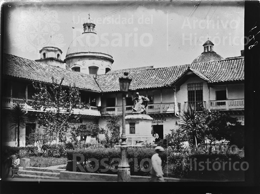 Plaza Rufino José Cuervo en Bogotá. En la mitad de la plaza se encuentra la estatua de Cuervo, obra de Charles Raoul Verlet, instalada en 1914. Detrás de la estatua de Cuervo, se ve un local comercial abierto con el letrero "Peluquería San Ignacio”, nombre que seguramente recibió de la iglesia que se ubica en frente.